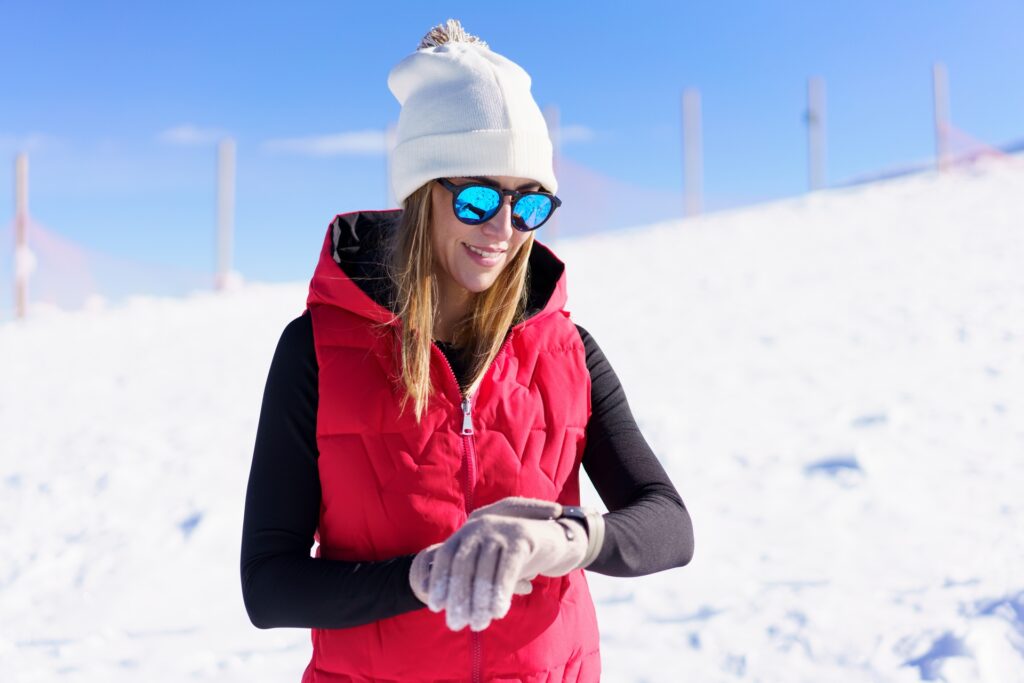 Ragazza bionda sorridente sulla neve con occhiali da sole con lenti polarizzate azzurre
